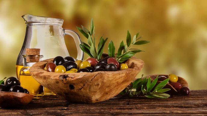 Image of glass bottles filled with quality cooking oil and some olives and herbs to infuse oil in a wooden bowl