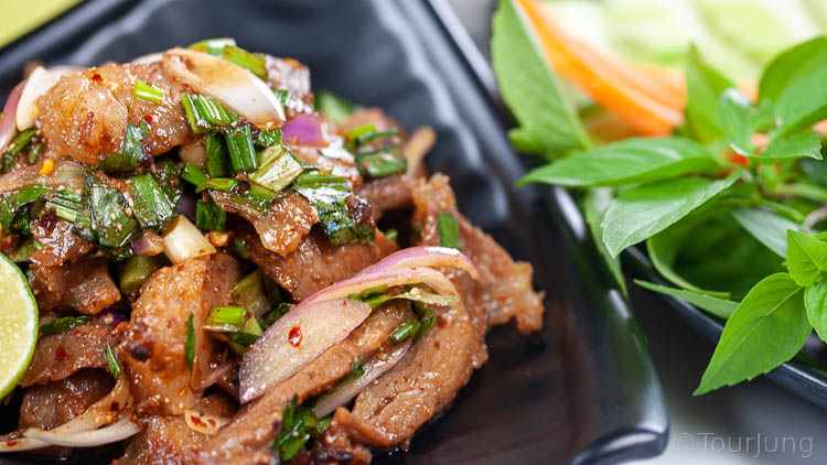 Easy Thai Beef Salad Recipe - Nam Tok Nua Close up photo of Thai beef salad recipe served on a black plate with side plate of fresh herbs