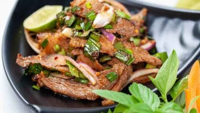 Photo of authentic Thai beef salad recipe served with fresh herbs and sticky rice out of picture