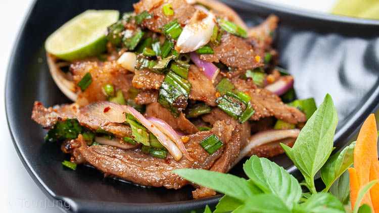 Photo of authentic Thai beef salad recipe served with fresh herbs and sticky rice out of picture
