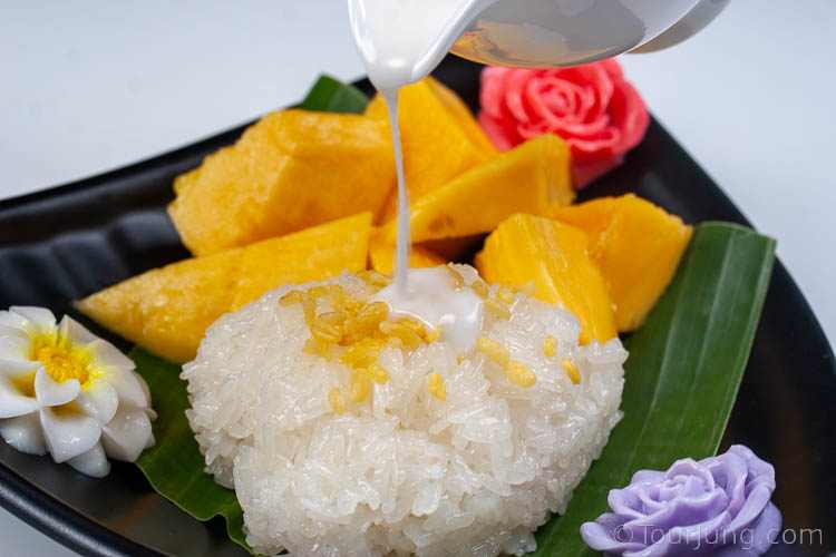 Photo of coconut milk dessert sauce being poured over sticky rice for mango