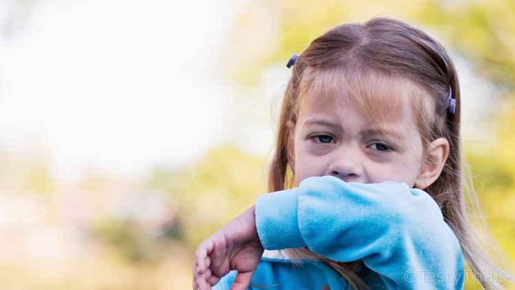 photo of small child coughing and sneezing into her arm