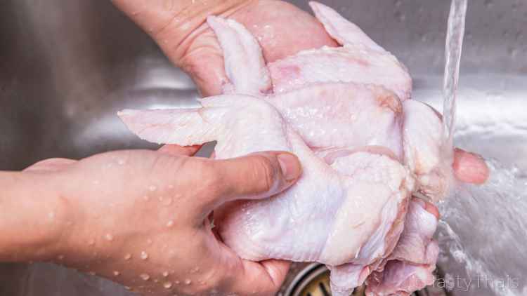 photo of uncooked fresh chicken wings being washed under running water.